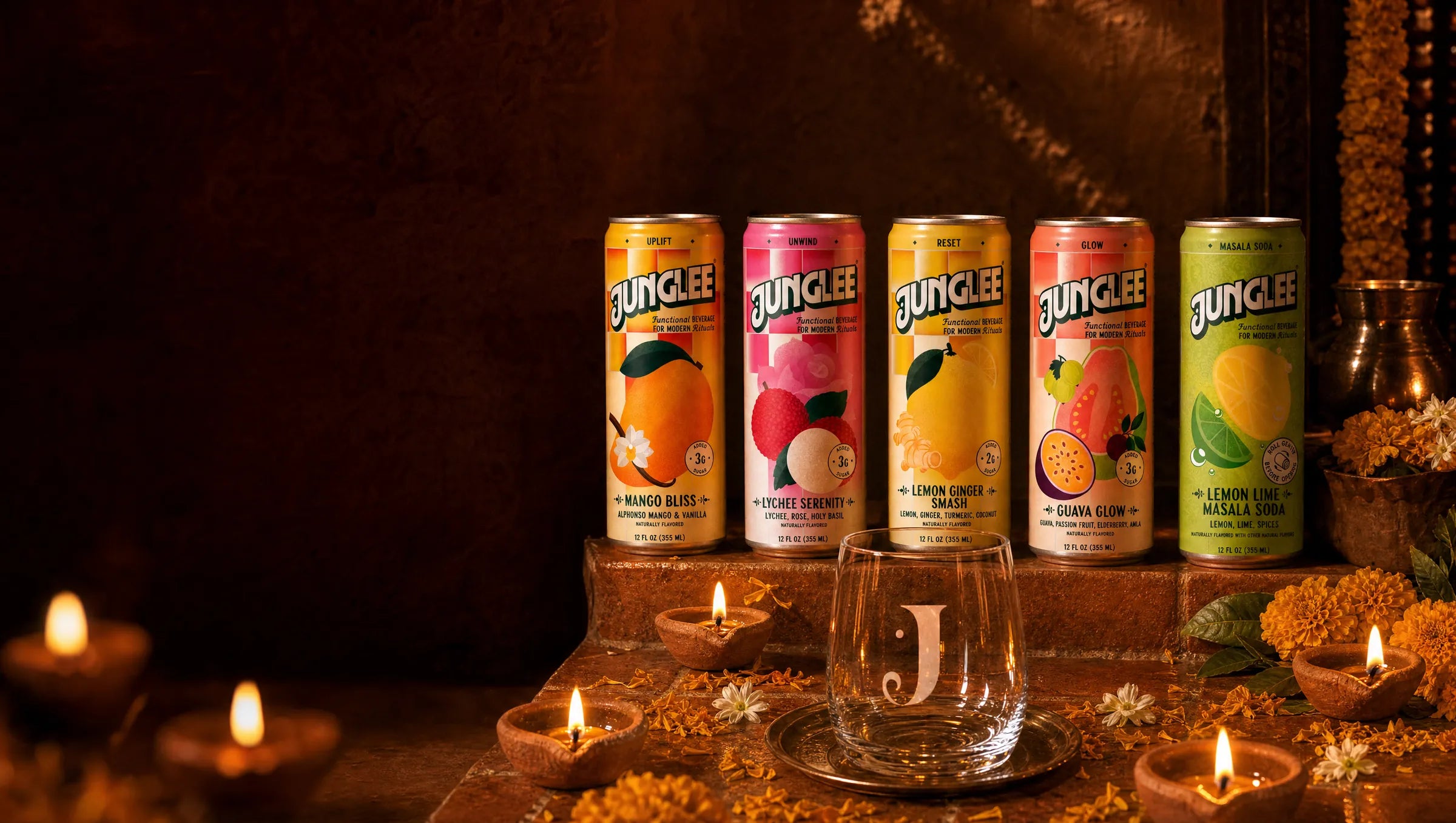All five Junglee cans on candlelit terracotta steps with the engraved Junglee J glass, glowing clay diyas and marigolds